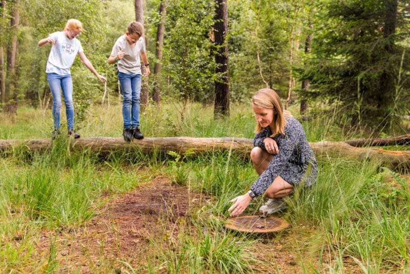Kinderen spelen in de natuur moeder zit gehurkt bij houten gedenkteken